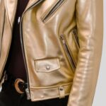 Nahaufnahme der goldenen Leder-Bikerjacke mit Reißverschlusstaschen, Druckknopf und Gürteldetail