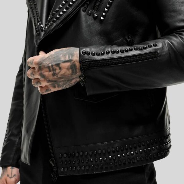 Nahaufnahme vom Ärmel und Saum einer schwarzen Lederjacke mit Nietenbesatz und Reißverschluss-Detail – Tattoo-Hand am Revers