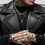 Nahaufnahme vom Revers einer schwarzen Nieten-Bikerjacke mit sichtbaren Tattoos, Halsketten und strukturiertem Leder