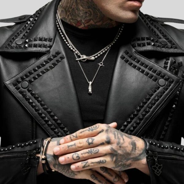 Nahaufnahme vom Revers einer schwarzen Nieten-Bikerjacke mit sichtbaren Tattoos, Halsketten und strukturiertem Leder