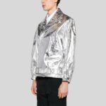 Seitliche Ansicht eines Mannes in glänzender silberner Metallic-Bikerjacke mit Gürtel, Reißverschlüssen und Reverskragen