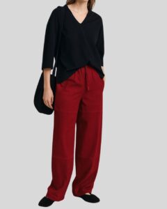 Frau trägt eine rote weite Wildlederhose mit Bindeband, kombiniert mit lockerem schwarzem V-Ausschnitt-Oberteil und Umhängetasche
