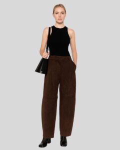 Frau trägt eine braune Wildlederhose in modernem Schnitt, kombiniert mit schwarzem ärmellosen Top, Umhängetasche und Stiefeletten