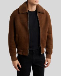 Herren trägt braune Suede Bomberjacke mit Shearling-Kragen, Reißverschluss und Rippbündchen, kombiniert mit schwarzem Shirt und Jeans